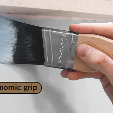 Hand holding a paintbrush with ergonomic grip on a white wall background